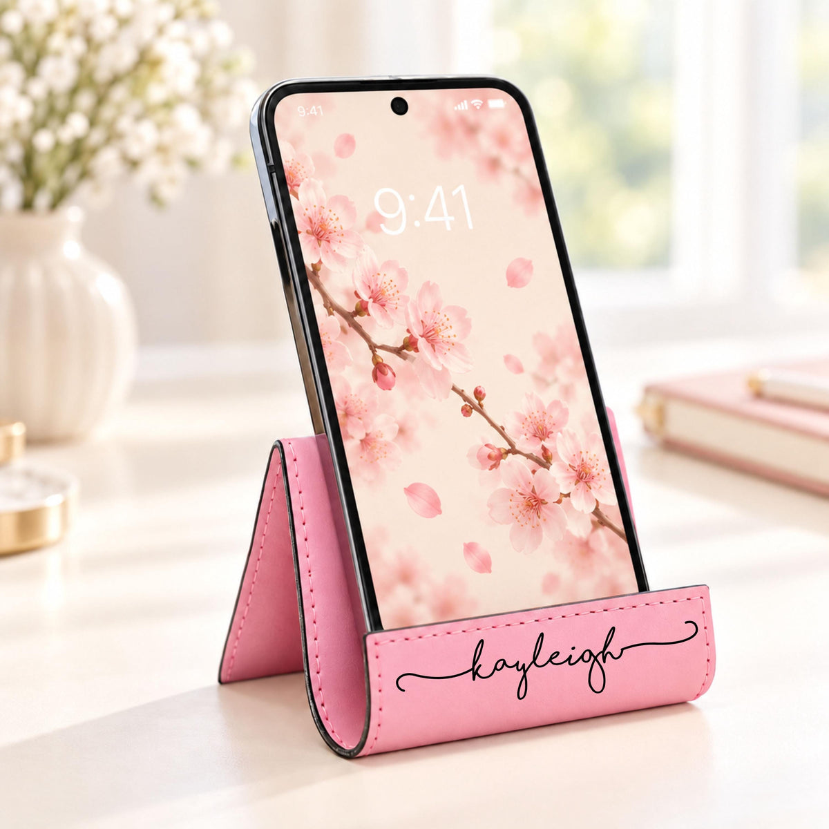 Personalized Leatherette Phone Stand in pink engraved with the name Kayleigh, holding a phone on a desk