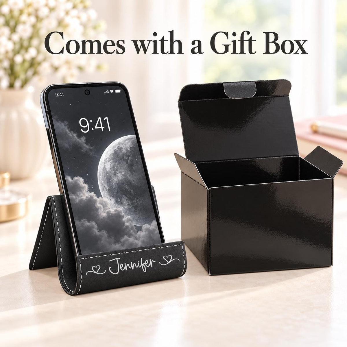 Black phone stand with silver engraving next to its black gift box